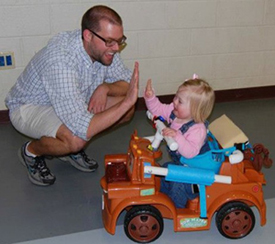 Todler in toy car giving high five to a councelor