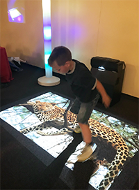 Child standing on top of a projected image of a leopard on the floor